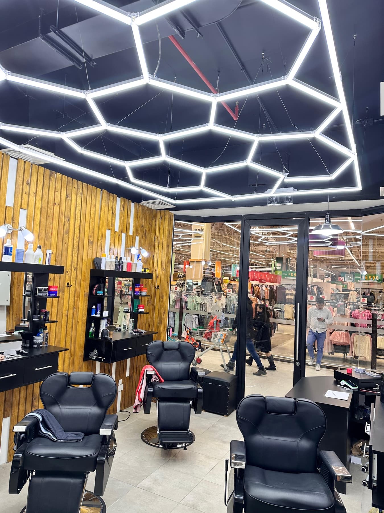 Interior de Barbería Montt: sillones negros, muros de madera y luces hexagonales en el techo