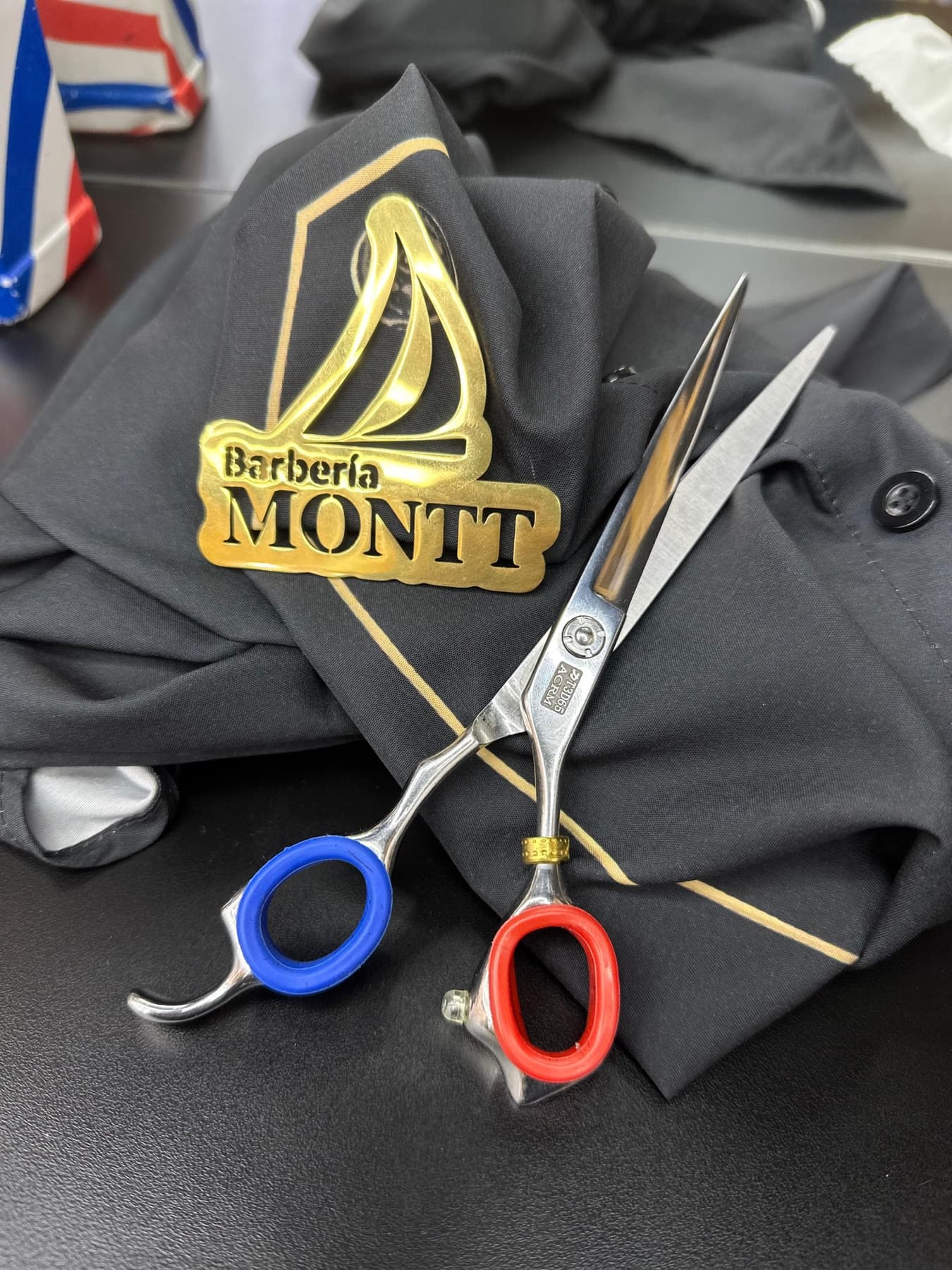 Tijeras sobre una capa con el logo dorado de Barbería Montt